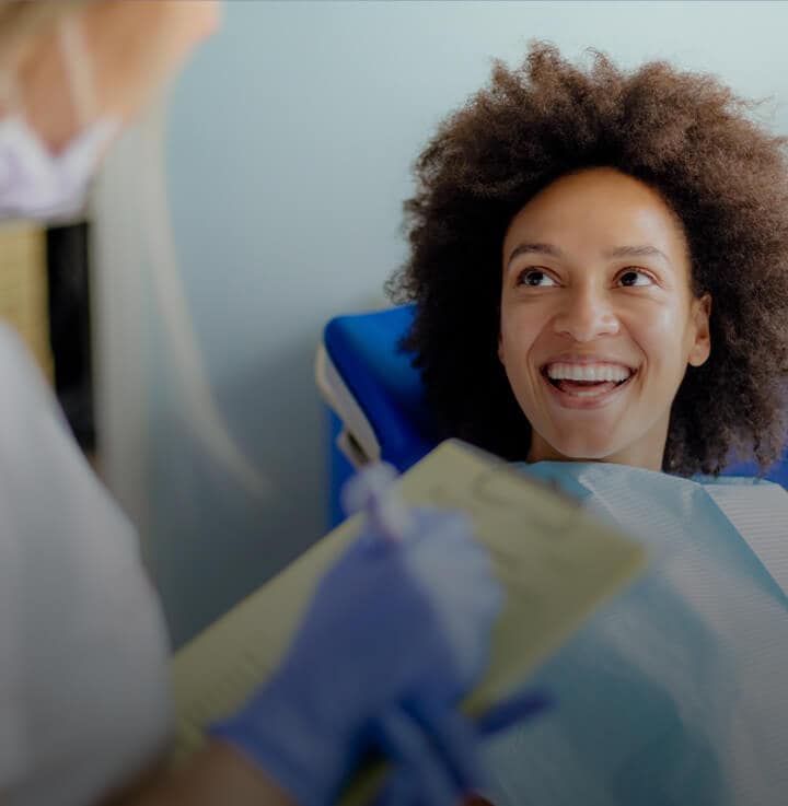 mujer con gran cabello rizado sentada en una silla de dentista y sonriendo mujer con gran cabello rizado sentada en una silla de dentista y sonriendo